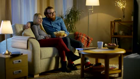 In-the-Evening-Man-and-Woman-are-Sitting-on-the-Sofa-Watching-TV-and-Eating-Popcorn.-Living-Room-is-Cozy.