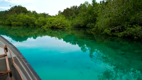 Hidden-Bay,-boat-moving-over-blue-shallow-water,-mangrove-reflection-on-calm-surface,-Raja-Ampat,-West-Papua,-Indonesia