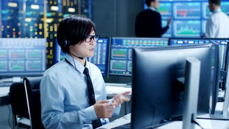 En-el-Network-Operations-Center-Trader-hace-cliente-Personal-llamada-con-auriculares.-En-los-comerciantes-de-fondo-discutir-datos-que-se-muestran-en-los-monitores.