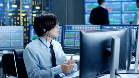 En-el-Network-Operations-Center-Trader-hace-cliente-Personal-llamada-con-auriculares.-En-los-comerciantes-de-fondo-discutir-datos-que-se-muestran-en-los-monitores.