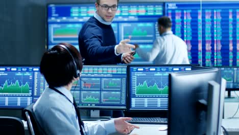 En-las-operaciones-de-red-Senior-Trader-dicta-números-de-Stock-a-su-operador-que-hace-llama-con-un-auricular.-En-los-comerciantes-de-fondo-discutir-datos-que-se-muestran-en-los-monitores.