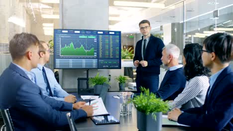 Young-Stock-Trader-Shows-to-the-Executive-Managers-Cryptocurrency-and-Trade-Market-Correlation-Pointing-at-the-Wall-TV.