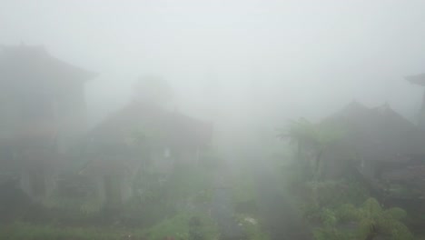 Aerial-Shot-Of-Abandoned-Balinese-Houses-And-Trees-Covered-With-Fog-4K