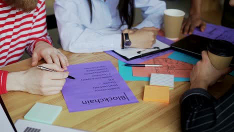 Closeup-of-male-hand-pointing-at-paper-with-plan-of-bitcoin-system-implementation-sharing-with-colleagues-sitting-at-the-table-and-discussing-start-up-project