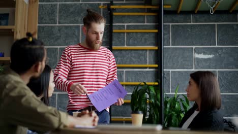 Young-hipster-male-leader-discussing-start-up-blockchain-project-with-multi-ethnic-team-showing-paper-plan