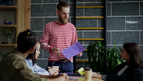 Young-hipster-male-leader-discussing-start-up-blockchain-project-with-multi-ethnic-team-showing-papar-plan