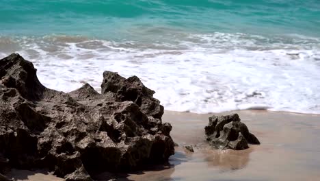 Las-olas-espumosas-lavan-las-rocas-corales-a-la-orilla-de-arena