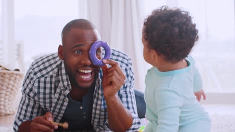 Padre-negro-joven-acostado-en-el-piso-jugando-con-su-hijo