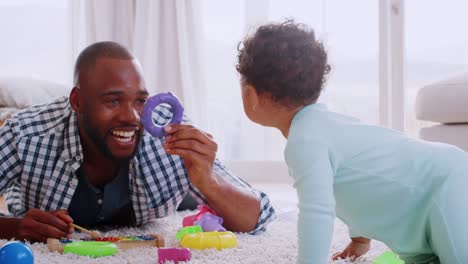 Padre-negro-joven-acostado-en-el-piso-jugando-con-su-hijo