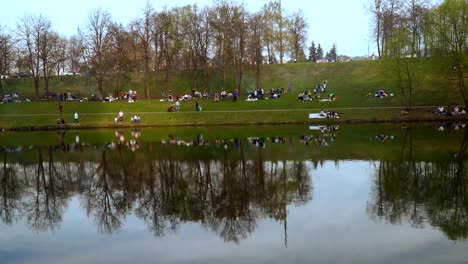 mucha-gente-en-un-picnic-de-la-primavera-en-la-orilla-de-la-laguna-de-la-ciudad,-lapso-de-tiempo