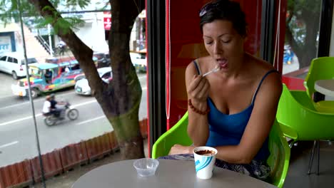 Una-mujer-en-un-café,-comer-un-helado-de-un-vaso-desechable