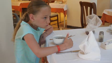 Adorable-chica-comiendo-gachas-de-avena-del-tazón-de-fuente-para-el-desayuno-en-la-cafetería