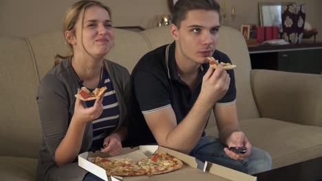 Attractive-young-couple-sitting-on-the-couch-and-eating-pizza