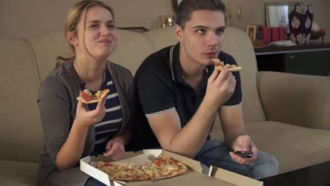 Attraktives-junges-paar-auf-der-Couch-sitzen-und-Essen-pizza