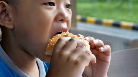 Close-up-little-asians-boy-enjoy-eating-burger,-Cute-happy-boy-holding-hamburger-at-restaurant.-video-Slow-motion