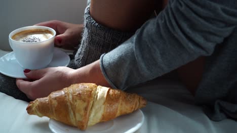 Mujer-sentada-con-la-taza-de-café-y-croissant-en-sofá-4K