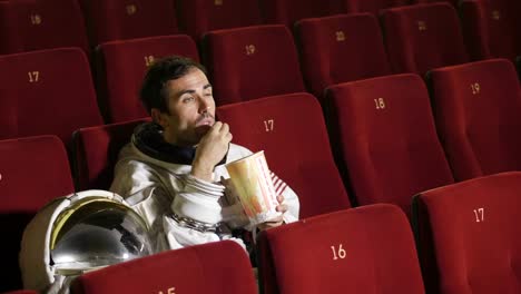 A-movie-astronaut-looks-at-a-movie-while-eating-pop-corn-and-enjoying-the-movie.-Concept-of:-cinema-and-space-films,-film-of-the-other-world,-surreal-situations.