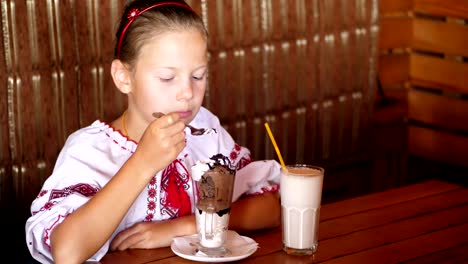 glücklich-lächelnd-Teen-Girl-Kind-isst-Eis-in-einem-Café.-Sie-ist-gekleidet-in-ukrainische-nationale-Kleidung,-Stickereien,-vishivanka