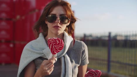 schöne-junge-glücklich-Frau-auf-der-Straße-mit-zwei-farbigen-Lollipop-bei-Sonnenuntergang