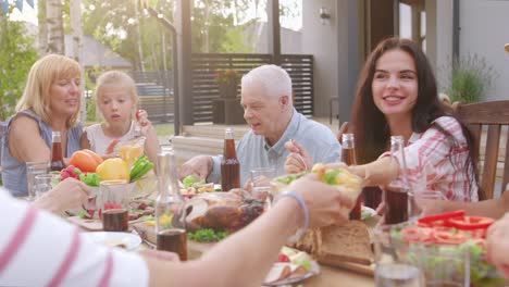 Gran-familia-jardín-fiesta-celebración,-reunidos-juntos-en-la-mesa-de-familiares-y-amigos,-jóvenes-y-ancianos-son-comer,-beber,-pasando-por-platos,-Joking-y-divierte.