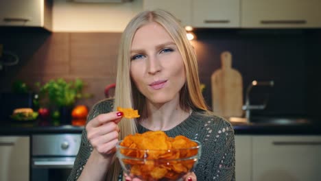 Mujer-alegre-comiendo-patatas-fritas.-Hermosa-mujer-joven-disfrutar-de-papas-fritas-y-mirando-a-cámara-mientras-está-sentado-en-la-cocina-con-estilo