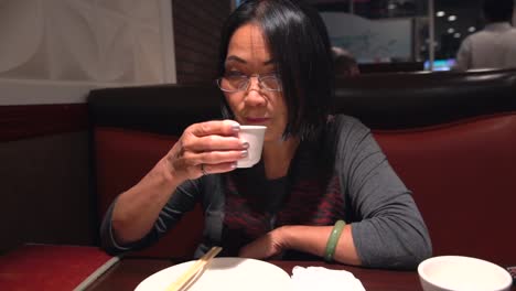 old-asian-woman-sipping-tea-at-a-restaurant