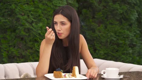 A-dolly-shot-of-a-young-pretty-brunette-eating-a-cake-sitting-outside.-She-eats-a-cake-in-little-pieces-looking-pensively