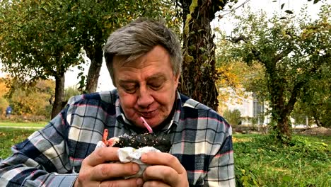 Hungry-adult-man,-in-casual-dress,-aged,-eats-hamburger-with-a-black-bun.