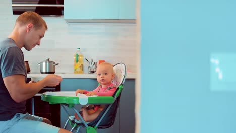 Hübscher-junger-Vater-Verfütterung-an-seine-Babynahrung-in-der-Küche