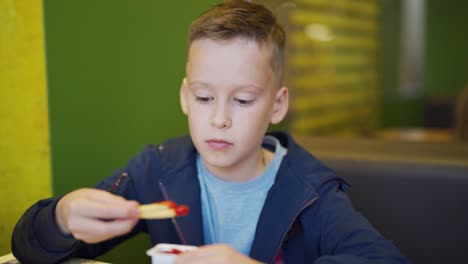 Niño-comiendo-papas-fritas-para-la-cena-en-cafetería-de-comida-rápida.