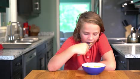 A-boy-eating-a-bowl-of-mac-and-cheese-at-home-in-a-kitchen.