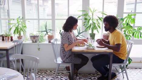 Middle-aged-mixed-race-couple-eating-lunch-together-at-a-table-in-a-restaurant,-close-up,-side-view