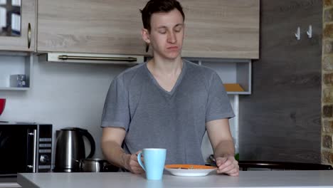 Young-man-eating-oatmeal-porridge-and-coffee-in-the-kitchen