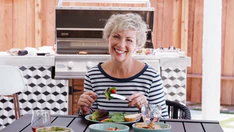 Ältere-Frau-beim-Mittagessen-in-den-Garten-mit-Blick-auf-Kamera