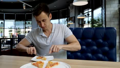 Young-handsome-man-eating-pizza-at-a-cafe