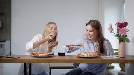 Zwei-schöne-junge-Mädchen-essen-Sushi-Rollen-und-reden,-Freunde-zusammen-in-der-Küche