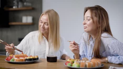 Dos-hermosas-chicas-comen-comida-japonesa-en-casa.-Rollos-en-una-placa-son-diferentes,-muy-sabrosos