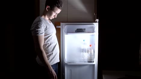 Young-man-eating-at-night-near-the-refrigerator