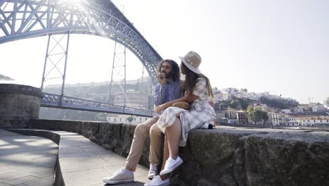 Couple-relax-on-embankment-near-bridge