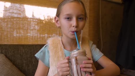 Portrait-teenager-girl-drinking-milk-shake-cocktail-at-table-in-cafe-close-up