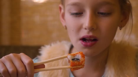 Young-teenager-girl-eating-sushi-roll-with-chopsticks-in-japanese-cafe-close-up