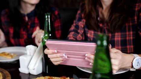 Vier-Mädchen-in-das-Restaurant,-das-Anzeigen-von-Fotos-auf-dem-Tablet.-Pizza-und-Bier-im-Restaurant.