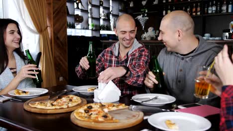 Company-of-cheerful-friends-at-the-table-of-the-restaurant-eating-pizza,-drinking-beer-and-having-fun-together.