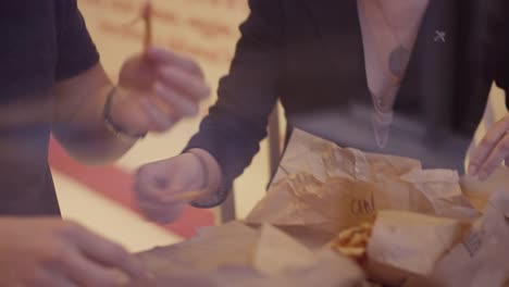 A-young-couple-laughing-and-eating-burgers-and-fries,-through-the-window