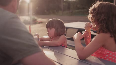 Zwei-Schwestern-Essen-Eis-mit-Ihrer-Familie-bei-einem-Picknick-Tisch