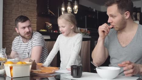 Little-girl-talking-with-same-sex-parents-at-breakfast