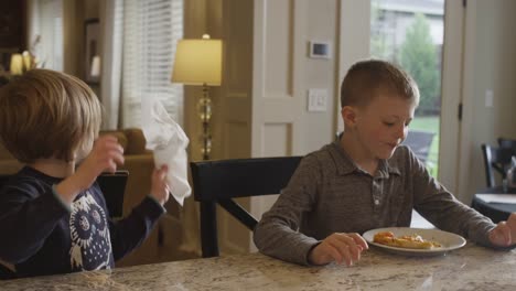 Brother-and-sister-sitting-at-a-kitchen-counter-and-eating-lunch-together