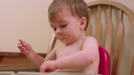 An-adorable-little-boy-in-a-high-chair-booster-seat-eating-messy-food-with-his-hands