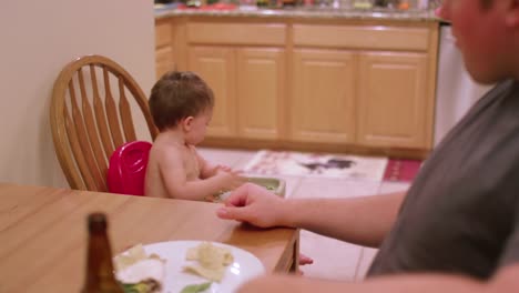 An-adorable-little-boy-in-a-high-chair-booster-seat-eating-messy-food,-dinner-time-with-family