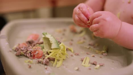 Close-up-of-a-baby-in-a-high-chair-booster-seat-eating-messy-food-with-his-hands